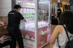 An event staff member restocks plush prizes inside a claw machine while guests wait nearby during a claw machine rental in Singapore event
