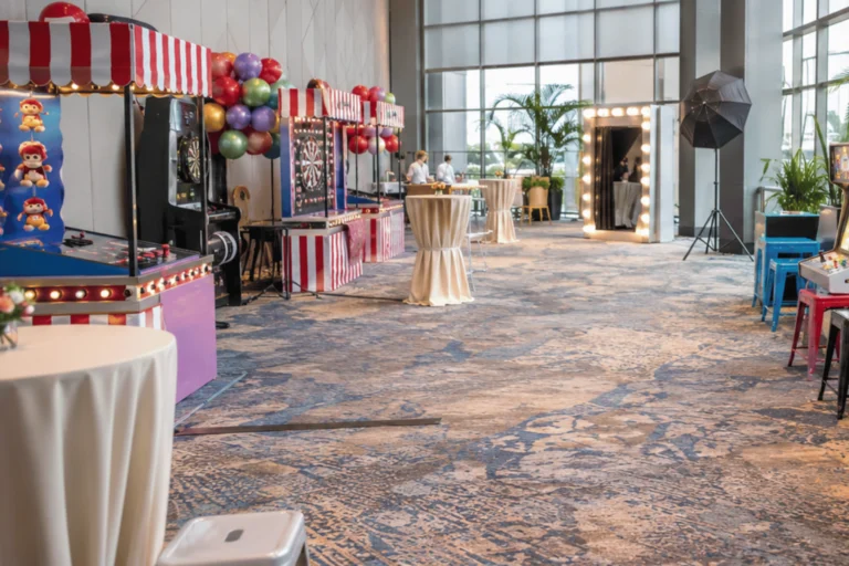 Event equipment rental in Singapore is arranged inside a modern corporate venue with arcade machines, carnival booths, a photo booth, and clear walkways for guests