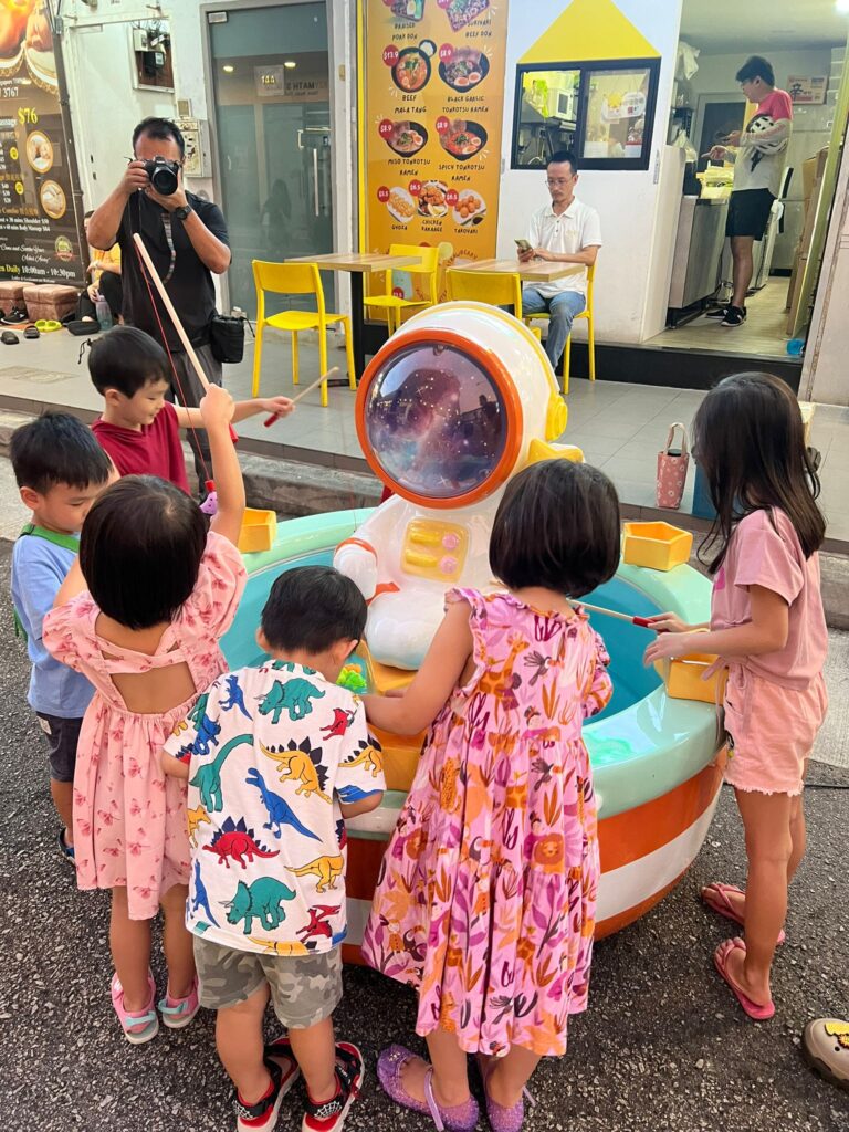 Children playing commercial 6-player large fishing carnival game stall during a corporate family day event in Singapore